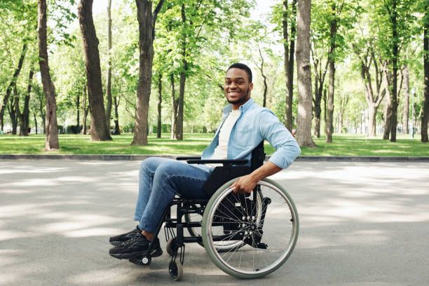 Smiling Black man in wheelchair outdoors, park setting.