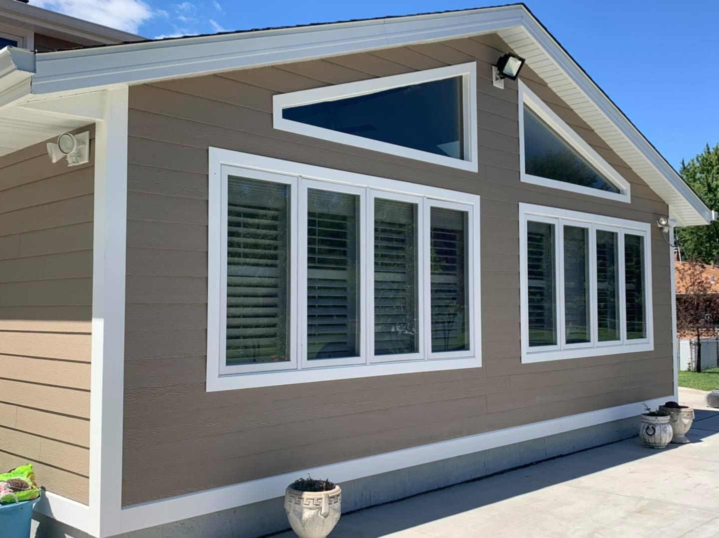 Taupe-colored exterior wall with white trim, large windows, and two triangular gable windows on a sunny day.