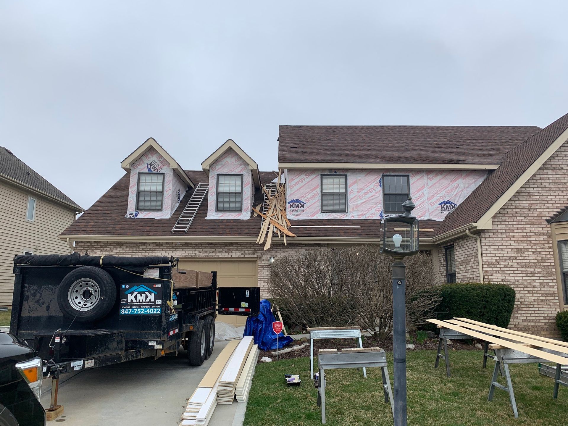 A house under exterior renovation with exposed wood framing, construction materials, and a dumpster in the driveway.