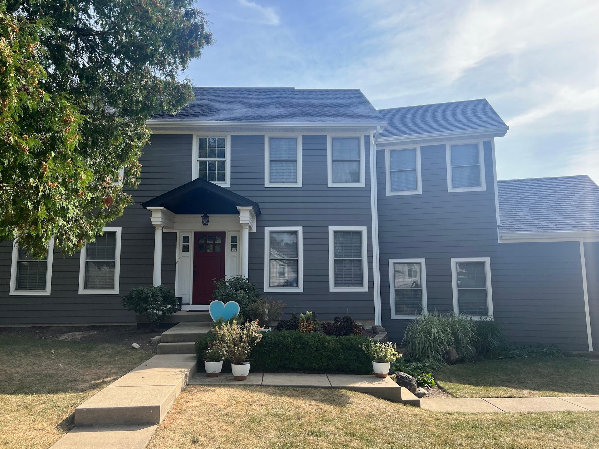 A two-story house with dark gray horizontal siding, a red front door, a dark roof, and a front walkway and garden.