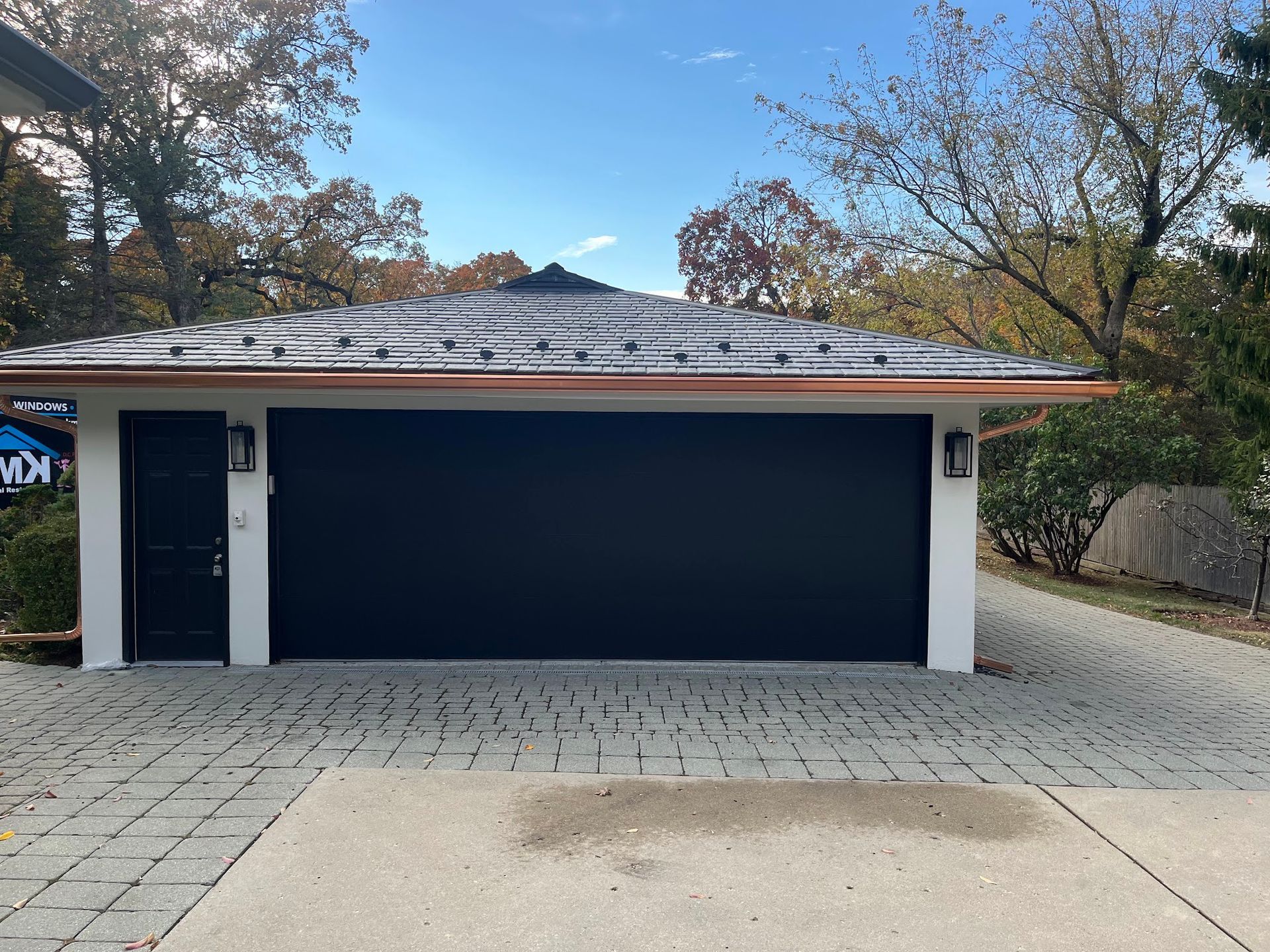 A detached garage with a white exterior, a black garage door and matching entry door, and a multi-faceted metal roof.