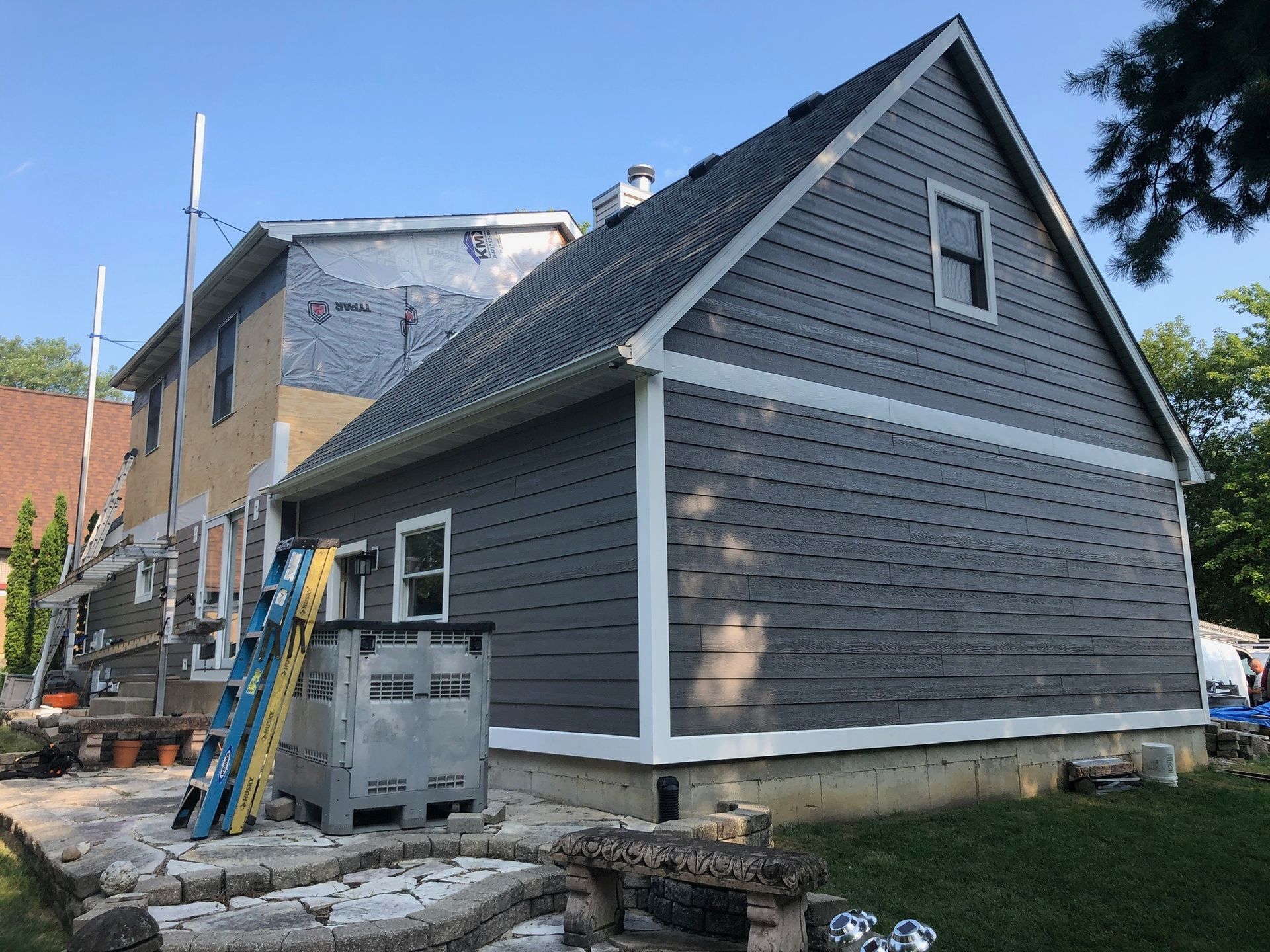 A house under renovation with dark grey siding partially installed and a blue ladder leaning against the structure.