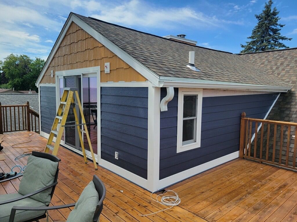 A renovated home addition with blue lap siding and brown shingles, featuring a sliding door, window, and wood deck.