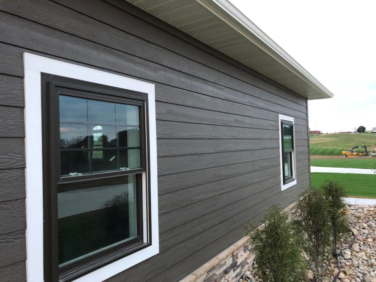 Dark brown horizontal siding on the exterior of a home with white-trimmed windows and a stone foundation.