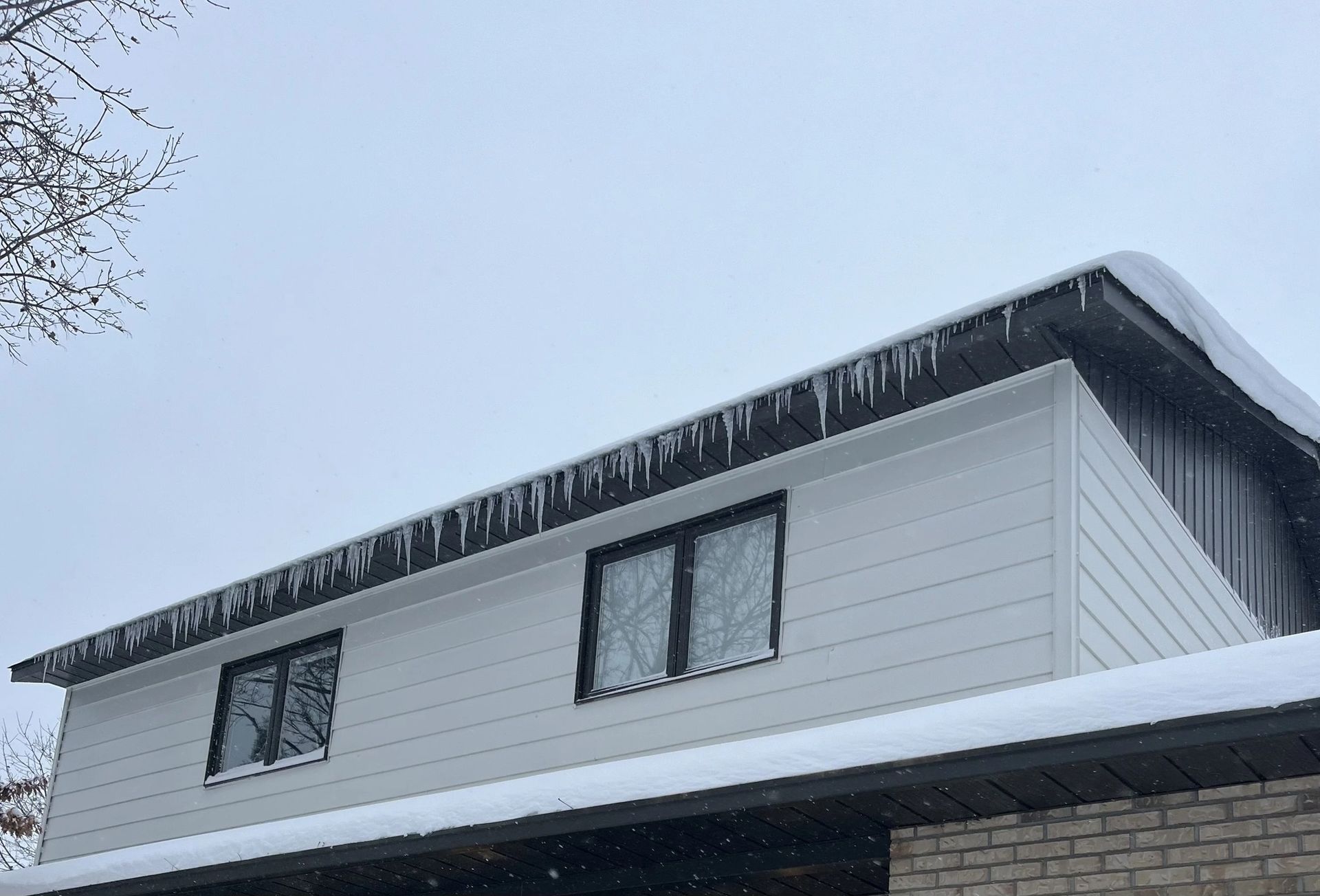 A side view of a white, two-story house with a row of icicles hanging from the roof overhang against a cloudy sky.