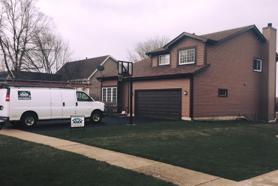 A white service van is parked in the driveway of a brown two-story house with a basketball hoop.