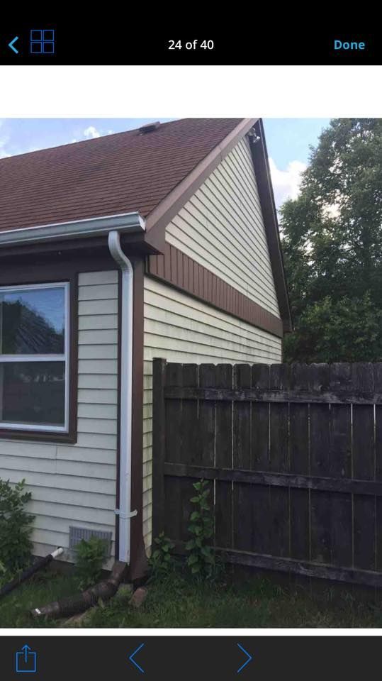 Side view of a light-colored house with dark brown trim, a red roof, a white gutter, and a wooden privacy fence.