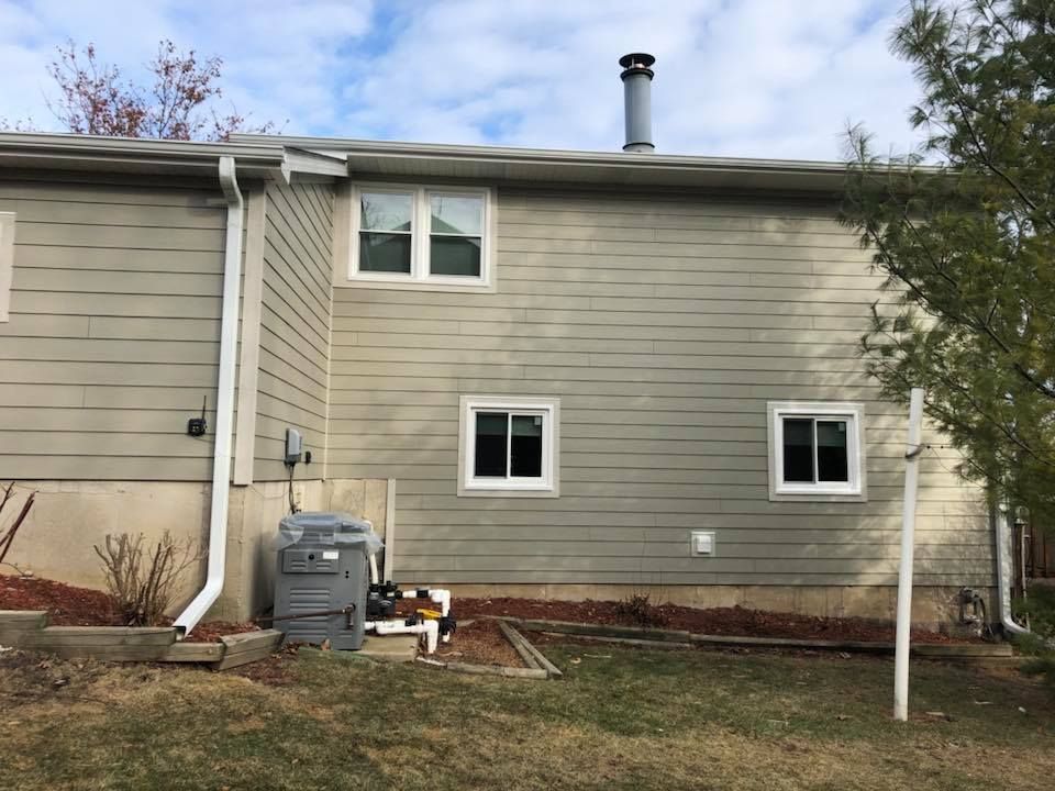 The side of a two-story home with light-colored horizontal siding, three white-framed windows, and an outdoor HVAC unit.