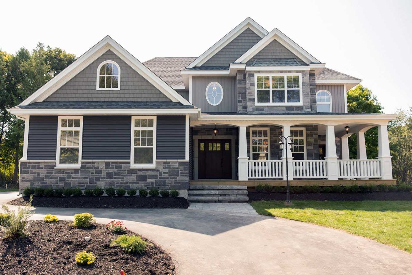 Two-story house with gray lap siding, stone foundation, white trim, a front porch, and a curved landscaped driveway.