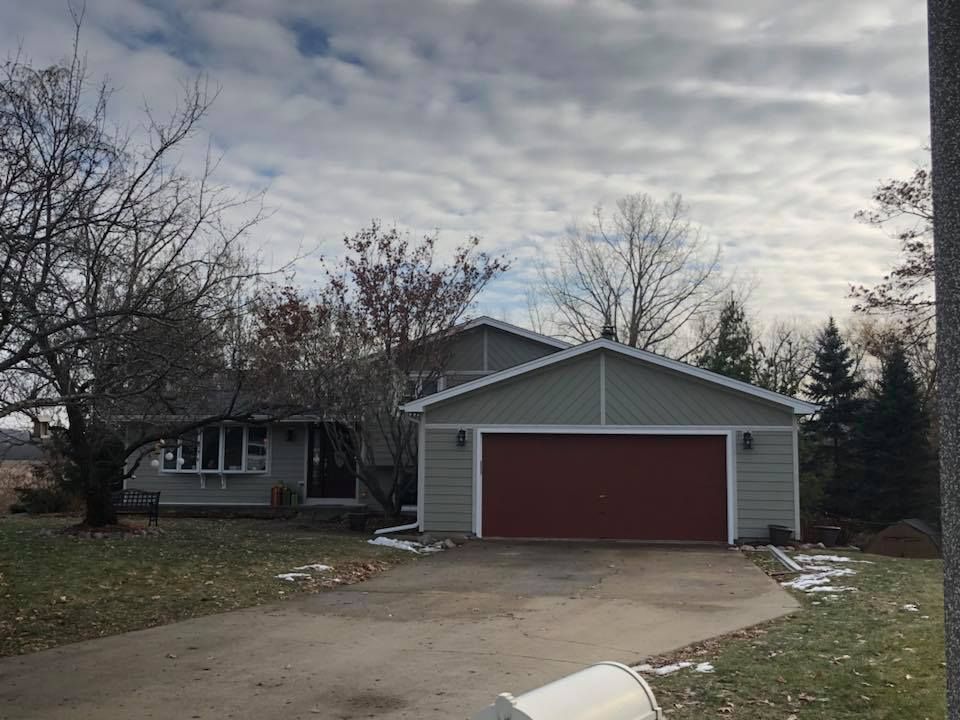 A one-story suburban home with light grey siding, a bright red garage door, and a bay window, under a cloudy sky.