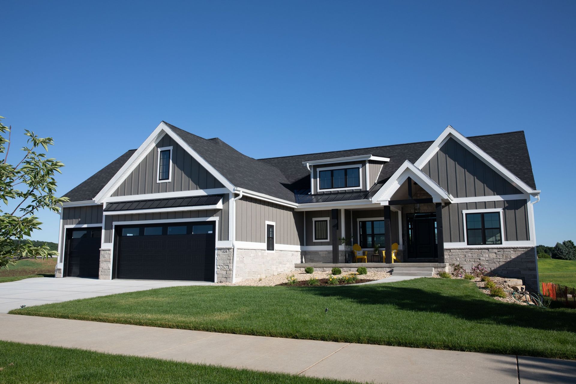 A modern, dark-gray house with white trim, a stone base, and a black garage under a clear blue sky.