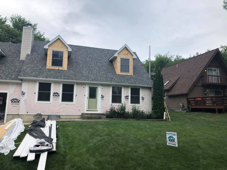 A light pink home undergoing exterior renovation, with exposed wood around the dormer windows and construction materials.