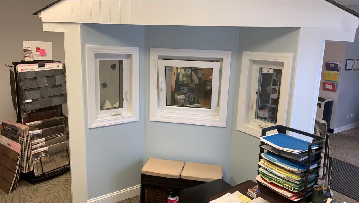 An indoor playhouse structure with light blue walls and three windows, featuring a bench inside and office supplies nearby.