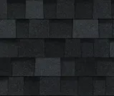 A close-up view of black architectural roof shingles with a varied, textured rectangular pattern.