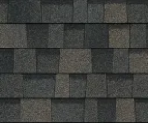 Close-up of overlapping asphalt roofing shingles in varying shades of charcoal, slate gray, and muted brown.