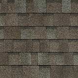 A close-up of dark brown and gray asphalt roof shingles with a multi-tonal, textured pattern.