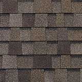 A close-up view of overlapping architectural asphalt roof shingles in varying shades of brown, tan, and dark gray.