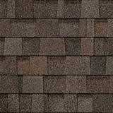 A close-up of brown and gray asphalt roof shingles with a varied, textured pattern.
