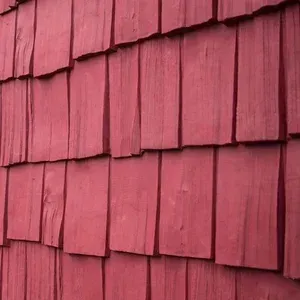A close-up view of dark red rectangular wooden shingles overlapping in a vertical pattern on a wall.