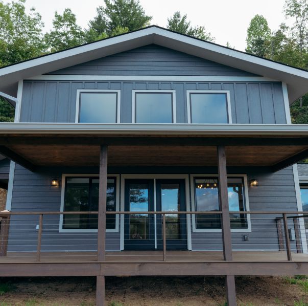 A two-story blue house with horizontal and vertical siding, featuring a covered deck and large windows under a gable roof.