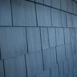Close-up view of grey, weathered rectangular wooden siding shingles arranged in a repeating, overlapping pattern.