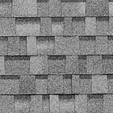A close-up of gray architectural roof shingles arranged in an overlapping, multi-textured pattern.