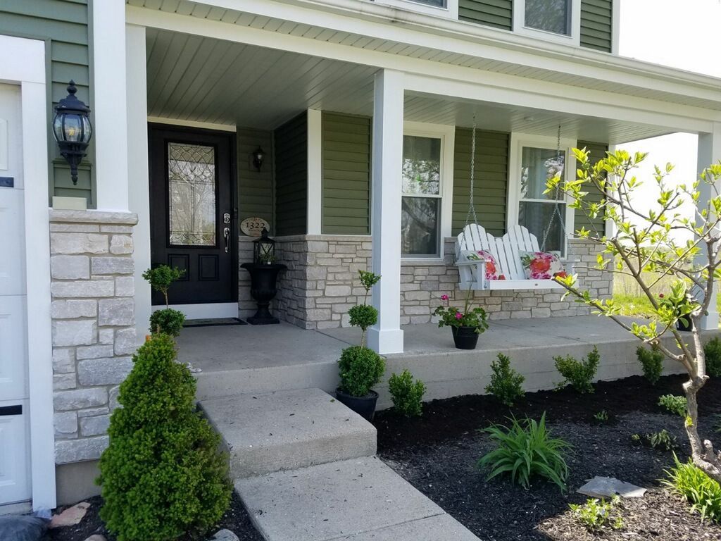 A front porch with sage green siding, light stone accents, a dark front door, and a white porch swing.