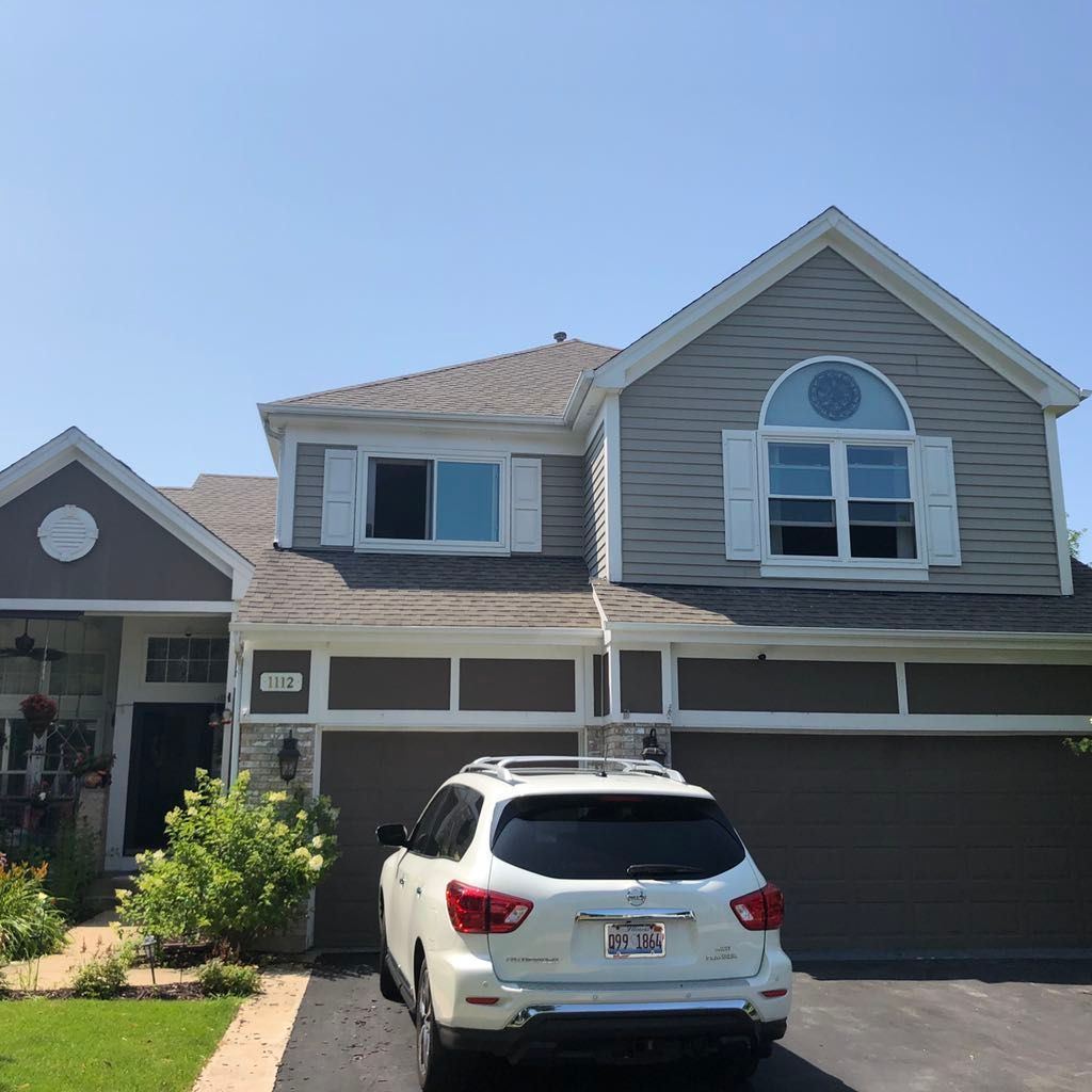 A two-story gray house with a driveway and a parked white SUV on a clear day.