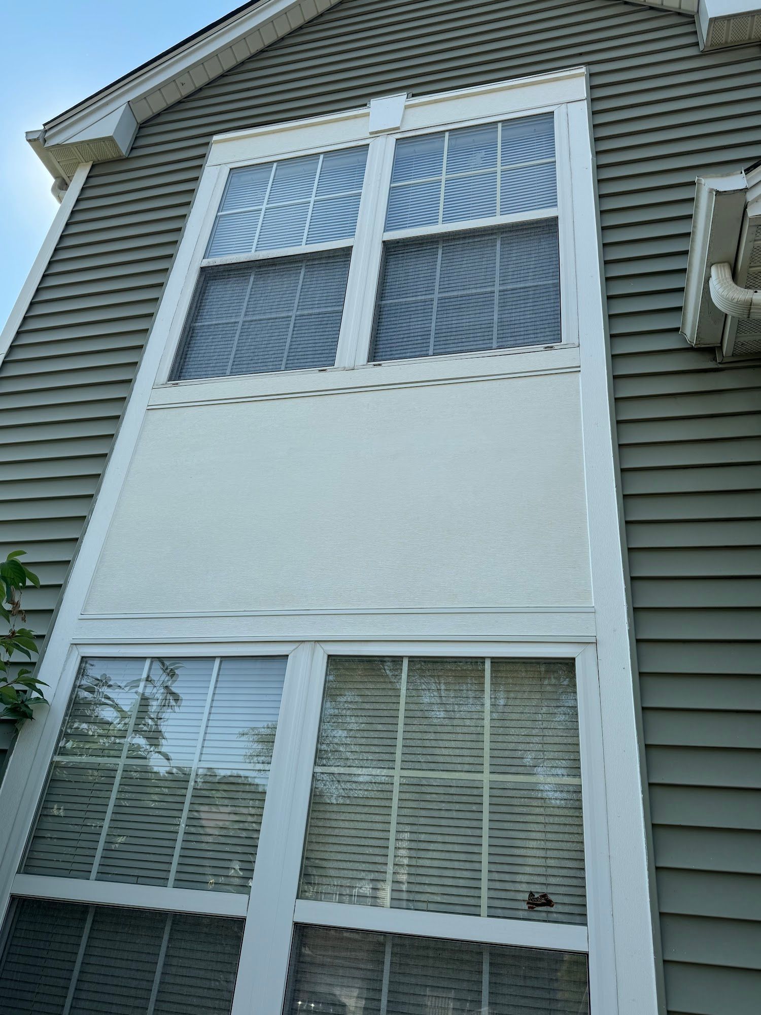 Exterior view of two large windows stacked vertically, separated by a white panel and bordered by gray siding.