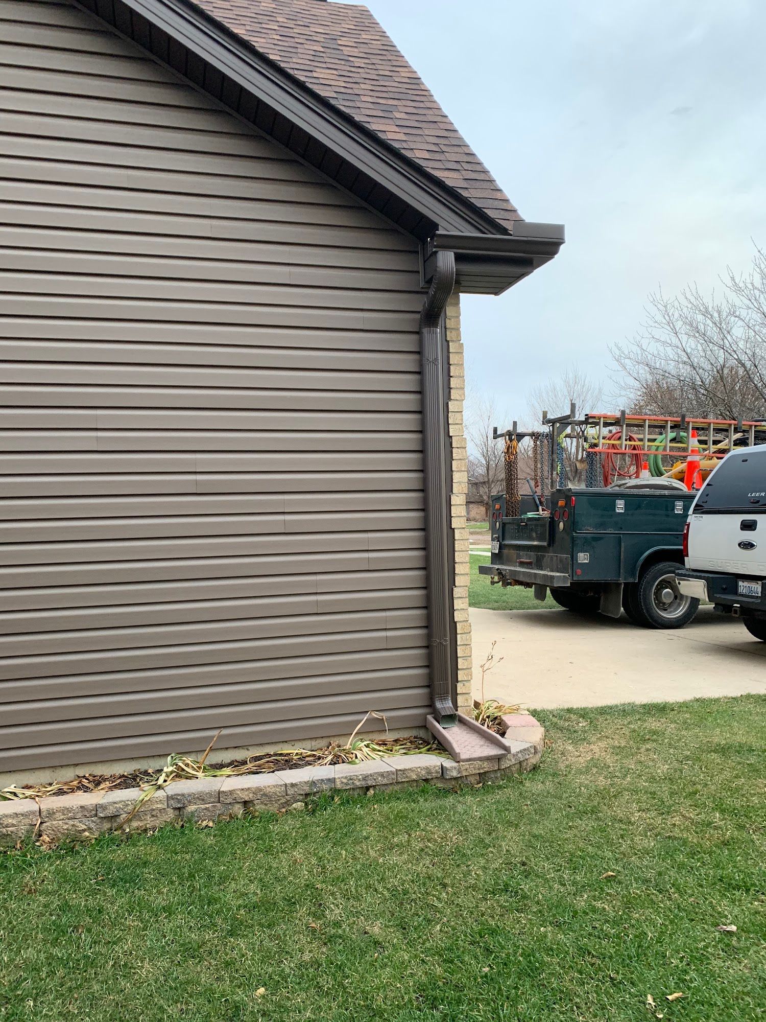 A side view of a house with brown vinyl siding, a dark downspout, and a utility truck parked in the background.