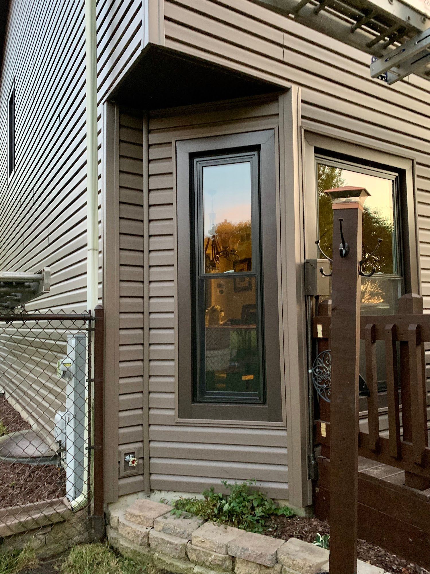 Exterior corner of a home with brown horizontal siding, a tall narrow window, and a stone planter base.