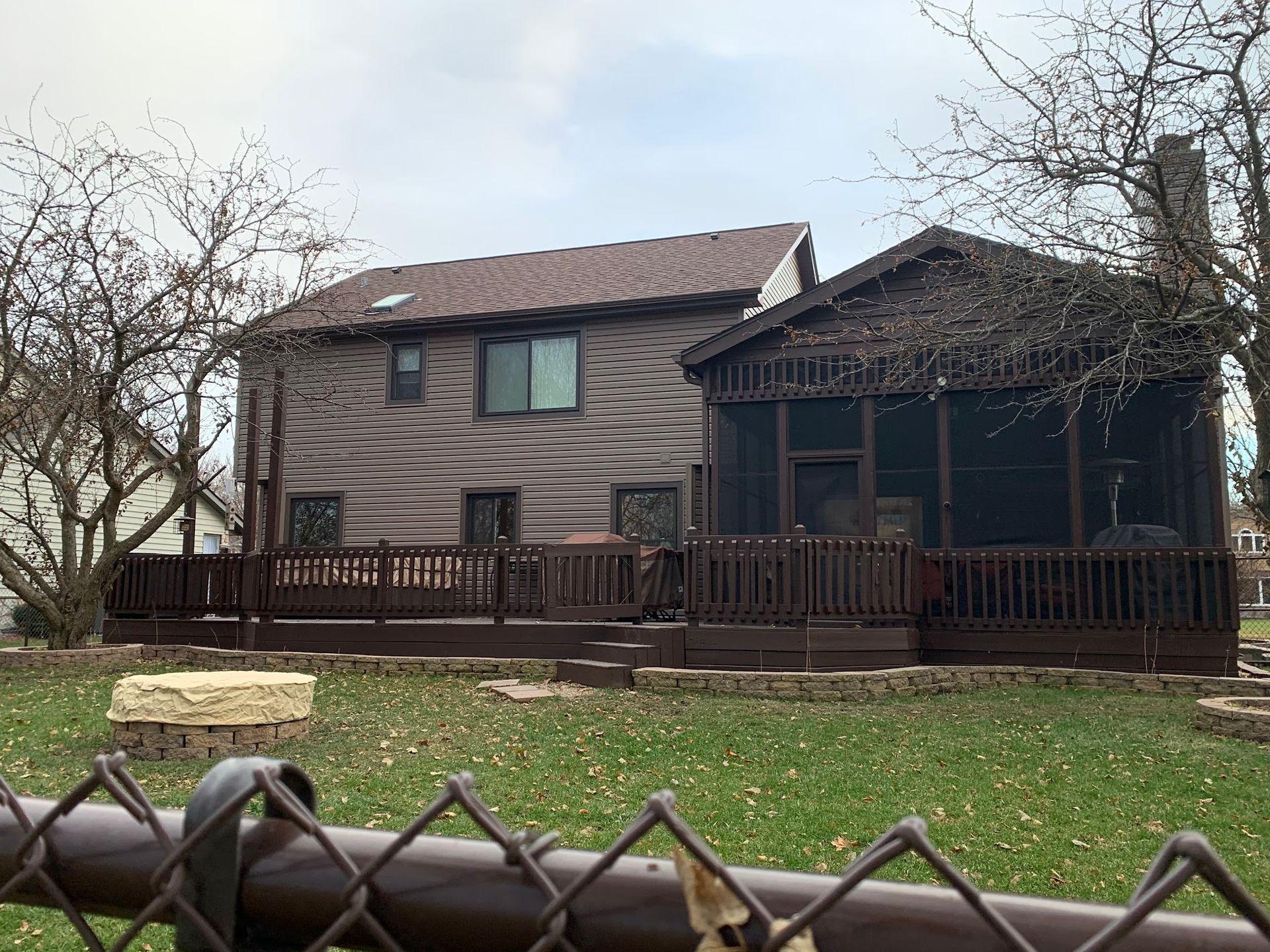 A two-story brown house with a large wooden deck and an attached screened-in porch, seen from a grassy backyard.