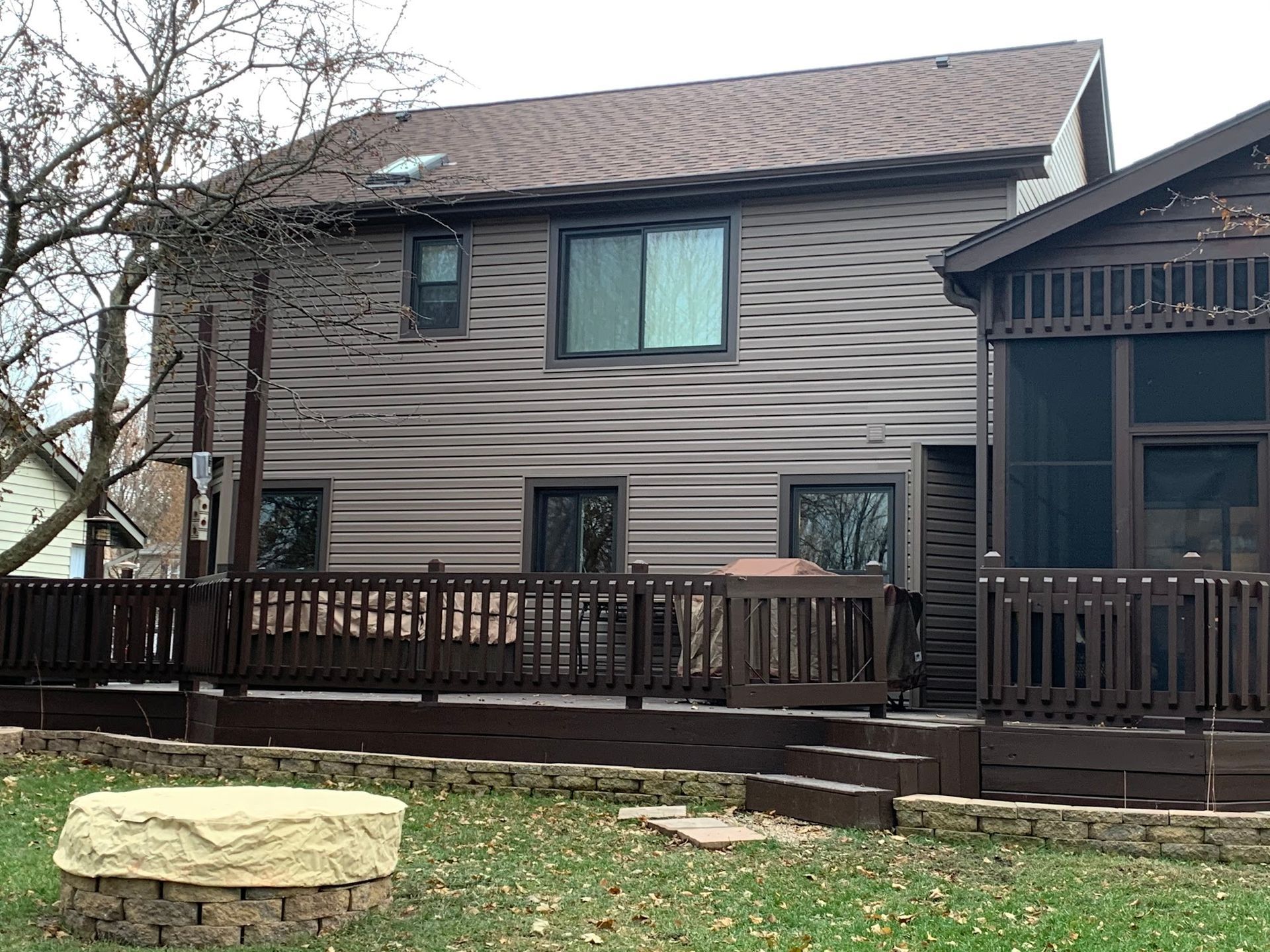 Brown house with horizontal siding, a deck, a screened-in porch, and a stone fire pit in the backyard.