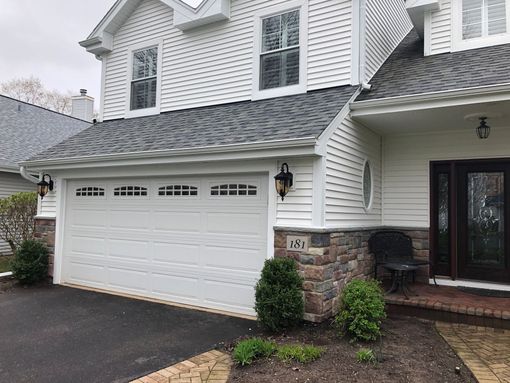 Two-story white house with a stone-trimmed front, a single-car garage, and a dark front door on a paved driveway.