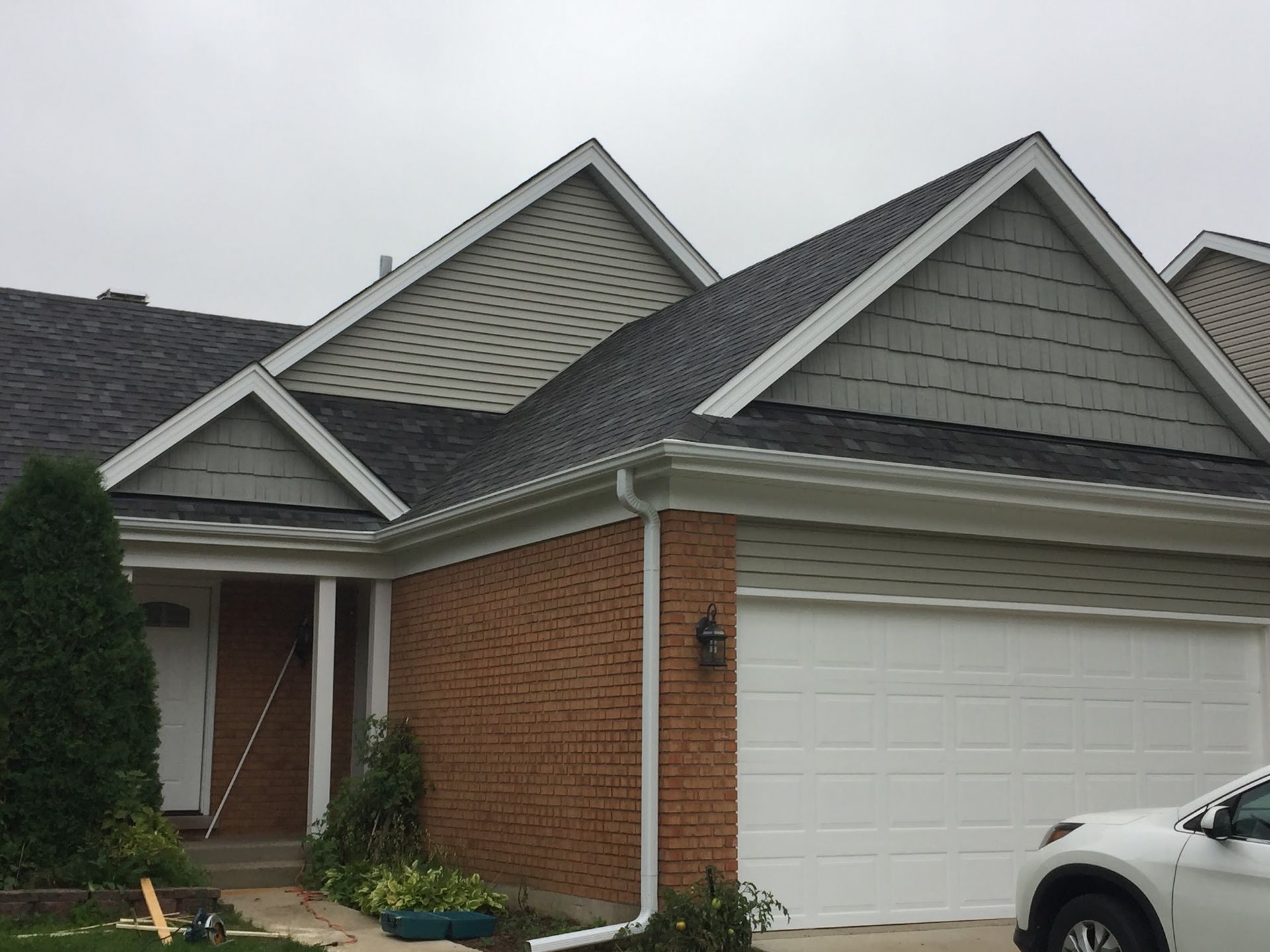 A house exterior featuring a brick ground level, white garage door, dark shingles, and grey siding on the gables.