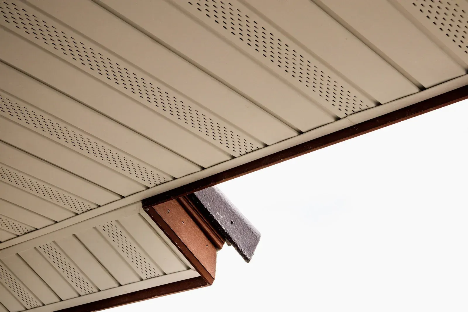 Low-angle shot of a house exterior showing a white gutter and soffit against gray siding under a clear blue sky.