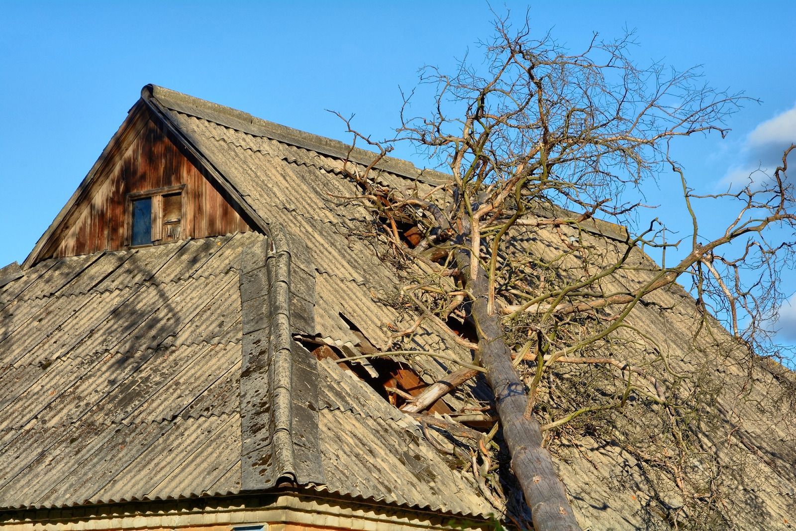 Exterior view of a tan brick house corner with a brown downspout and a stone-walled garden bed next to a lawn.