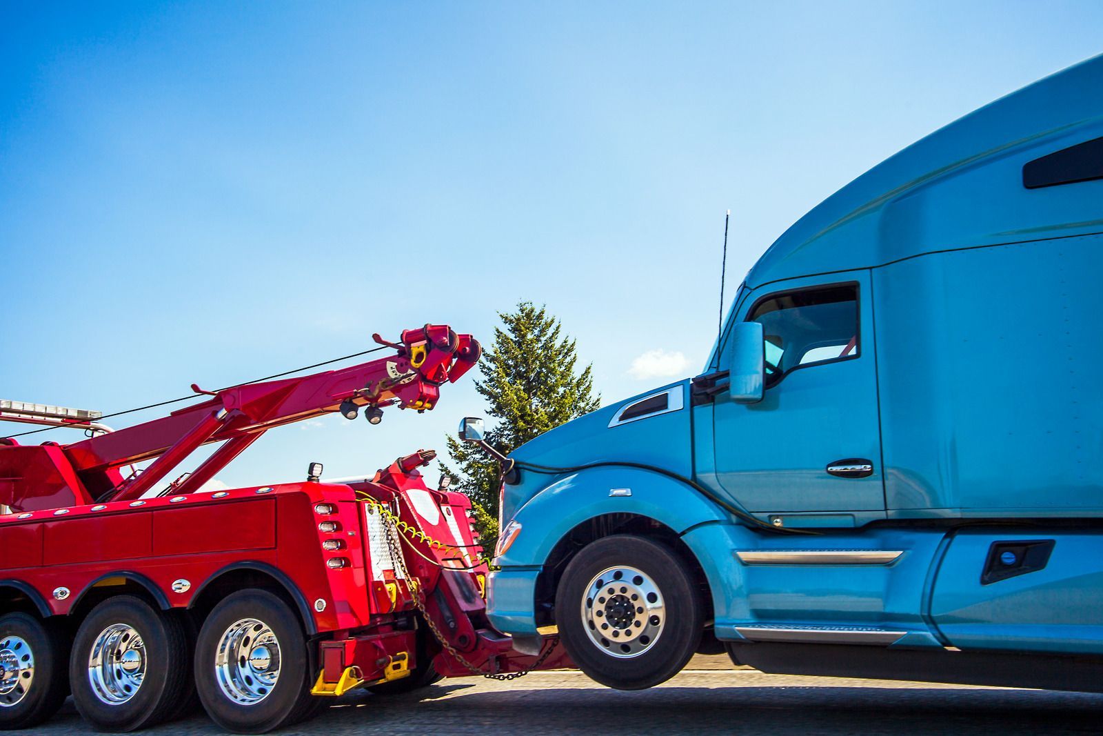 A blue semi truck is being towed by a red tow truck.