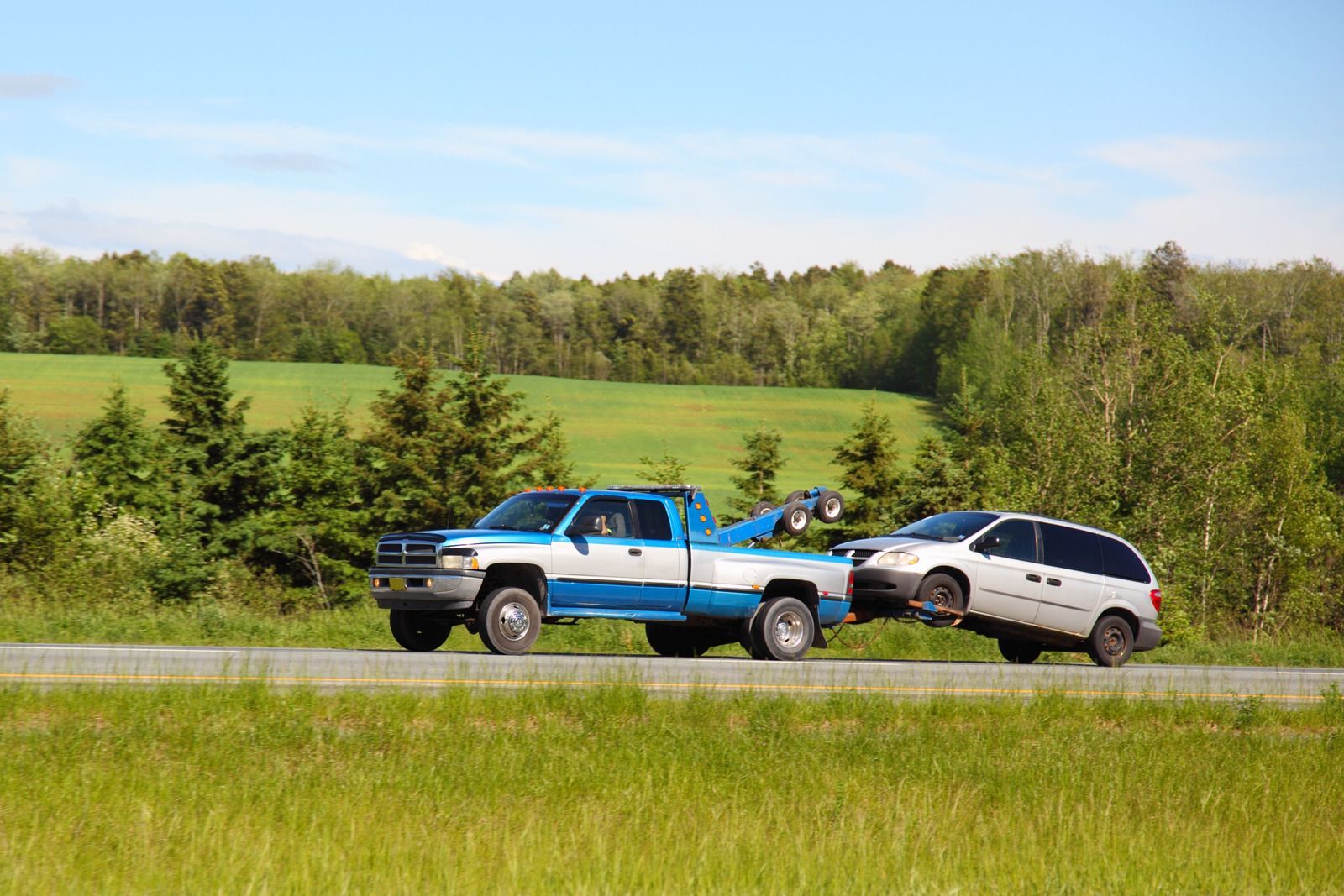 A blue and white tow truck is towing a white van down a road.