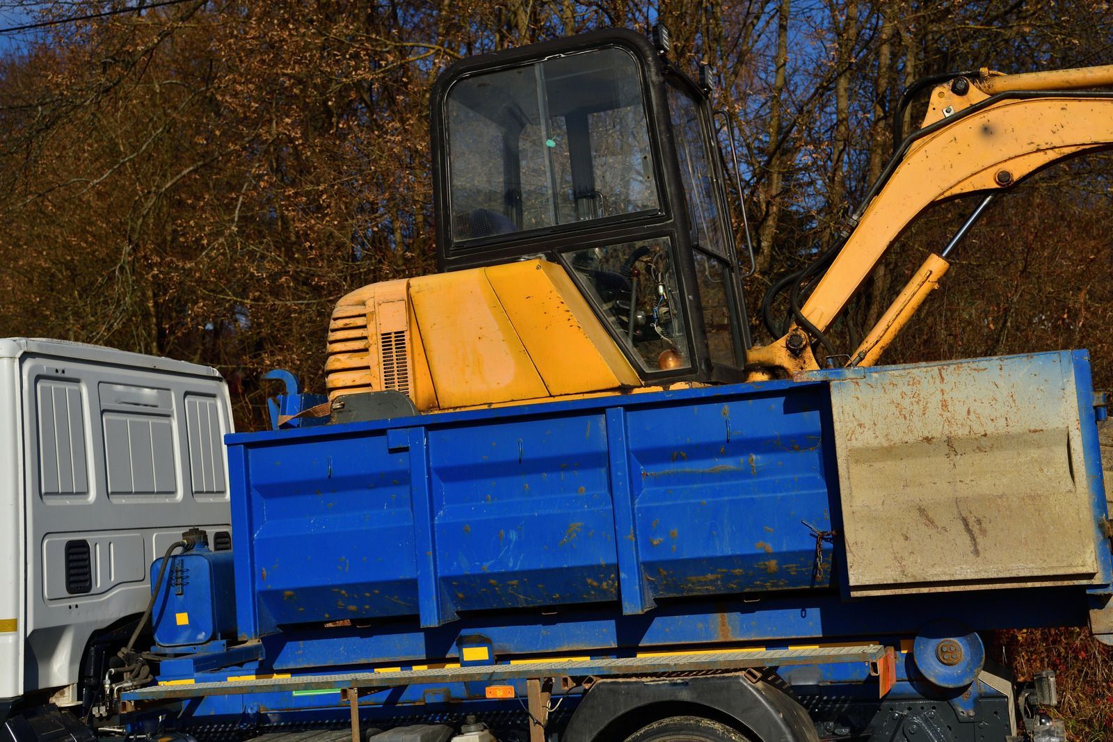 A yellow excavator is sitting on top of a blue dumpster.