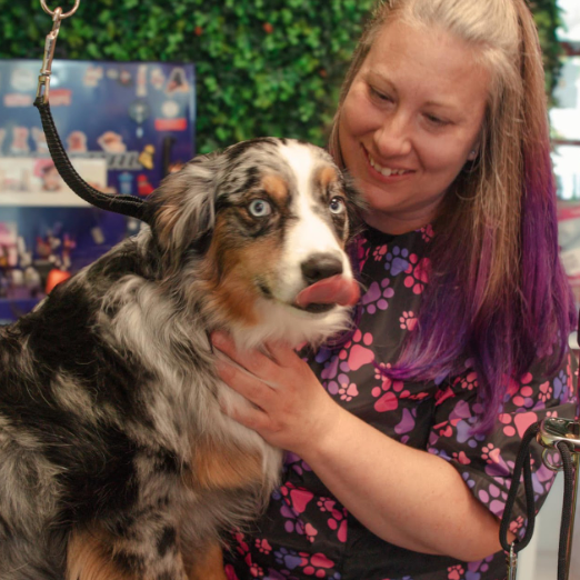 A woman with purple hair is holding a dog