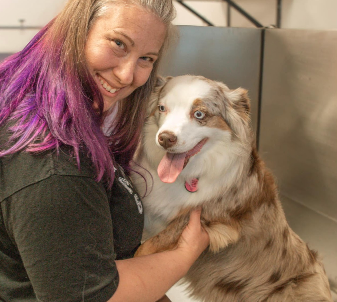 A woman with purple hair is holding a brown and white dog