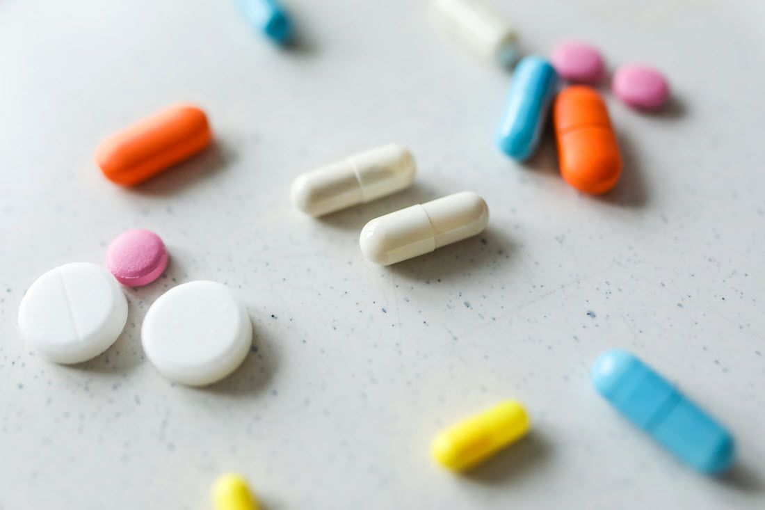 A scattering of various colorful tablets and capsules resting on a neutral, speckled surface.