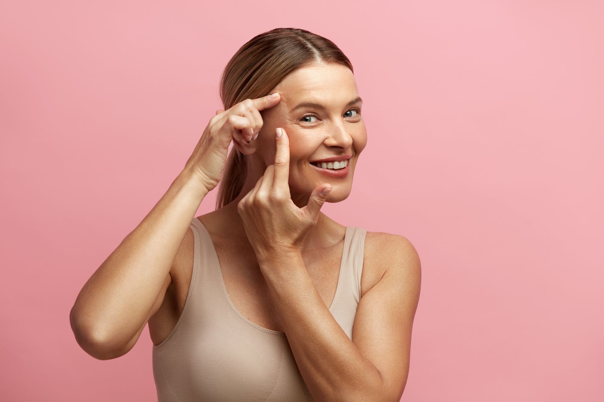 A woman is pointing at her face with her finger.
