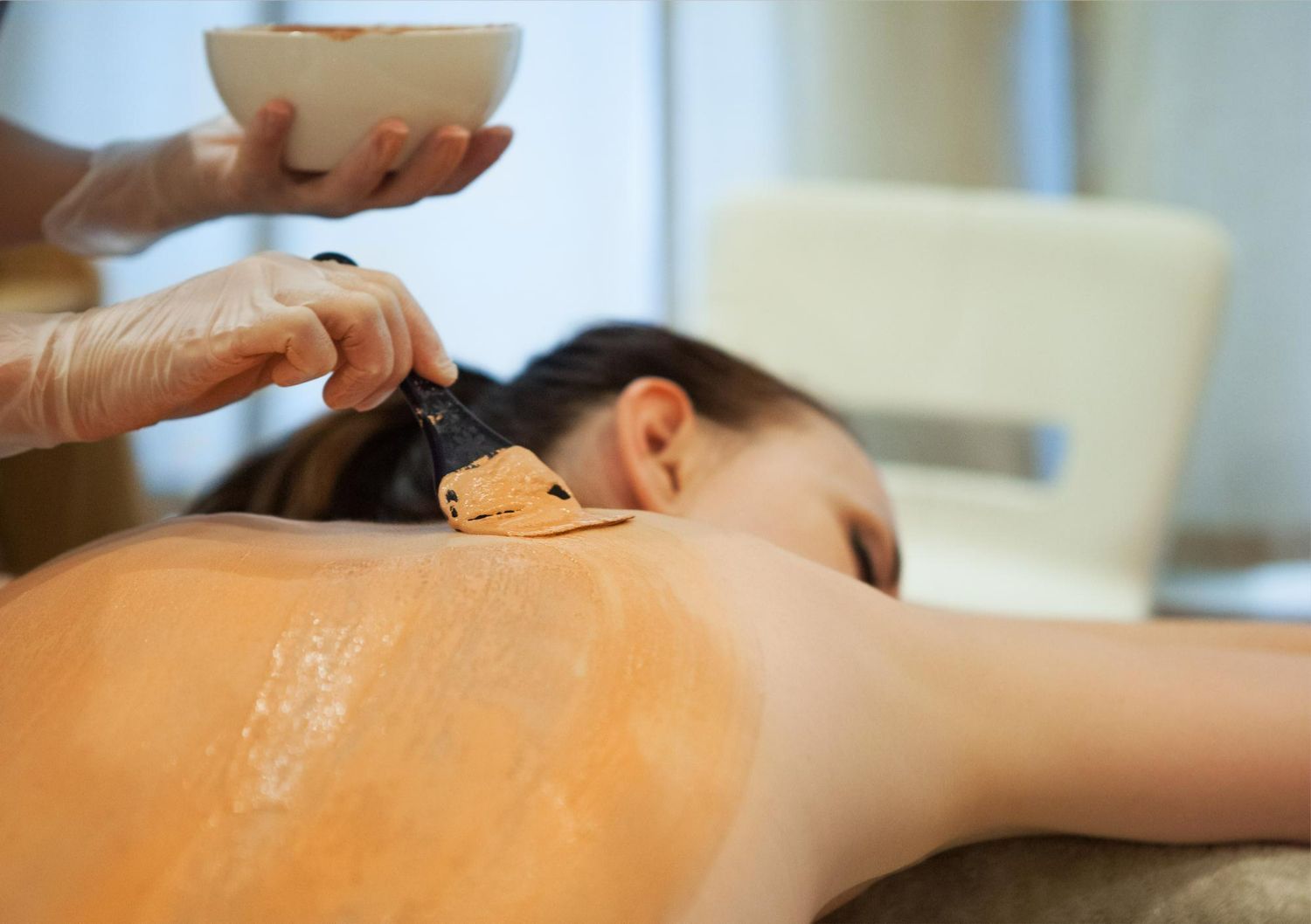 Therapist applying orange mask to a person's back at a spa.