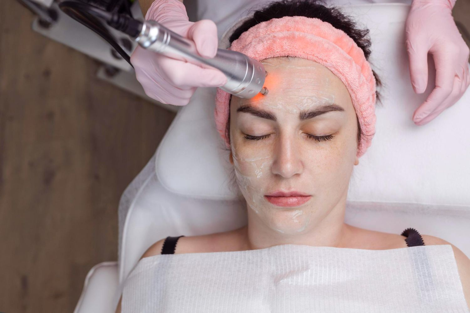 Woman receiving facial treatment with a device, red light, and cream applied.