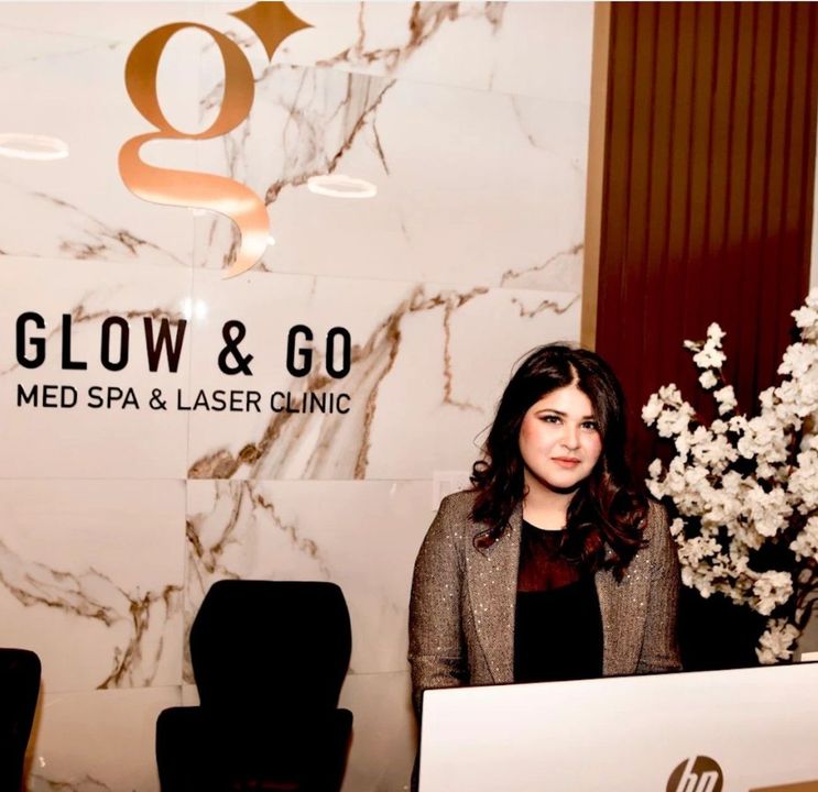 A woman sitting at a desk in front of a sign that says glow & go med spa & laser clinic