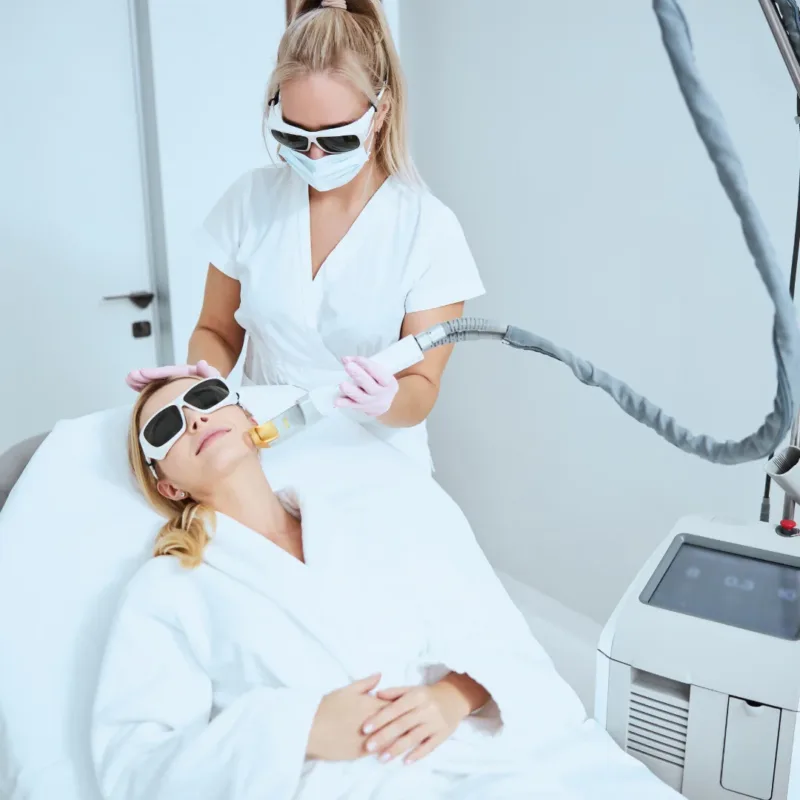 A woman wearing sunglasses is getting a laser treatment on her face