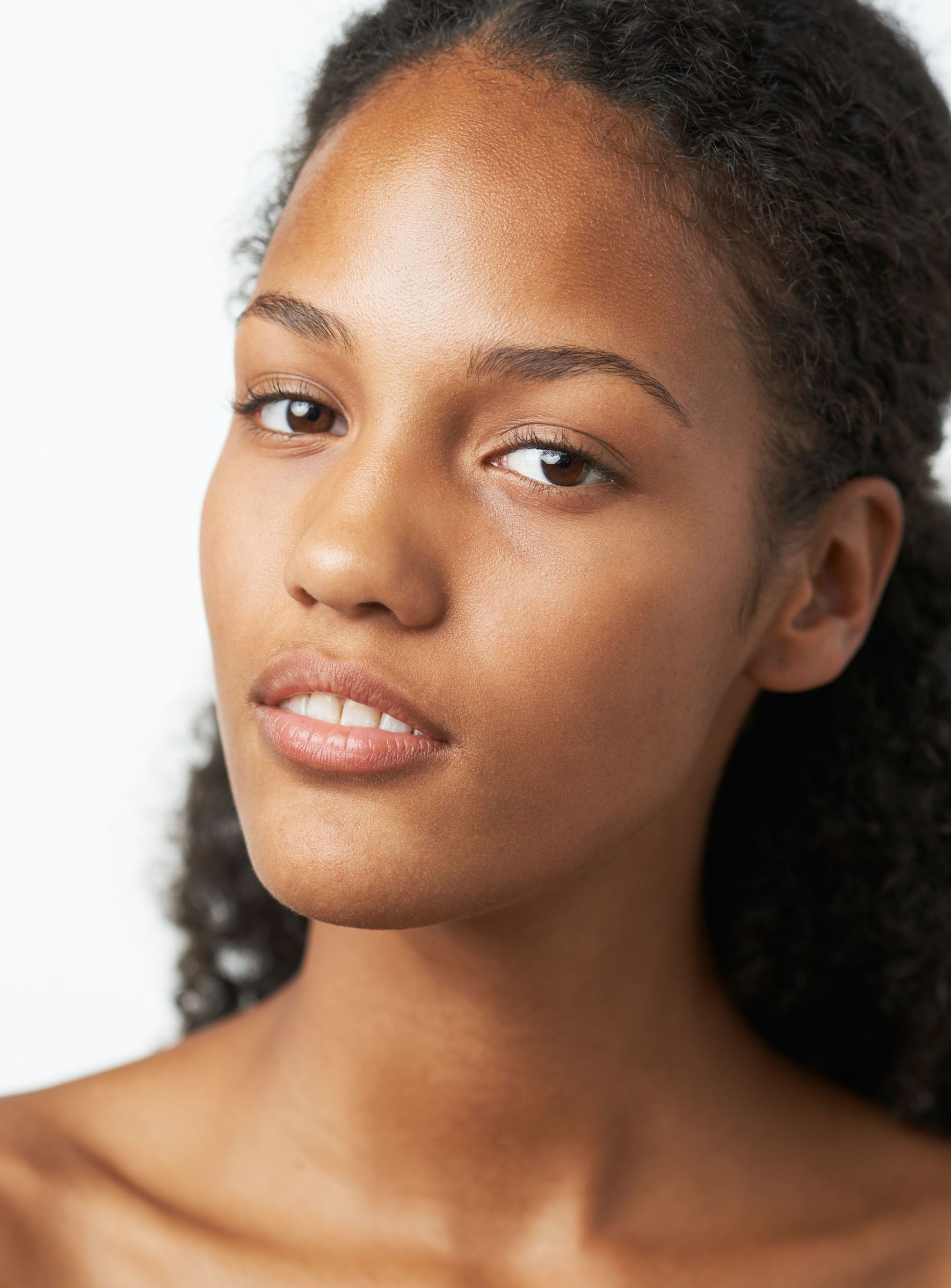 A woman with freckles is smiling and touching her face.