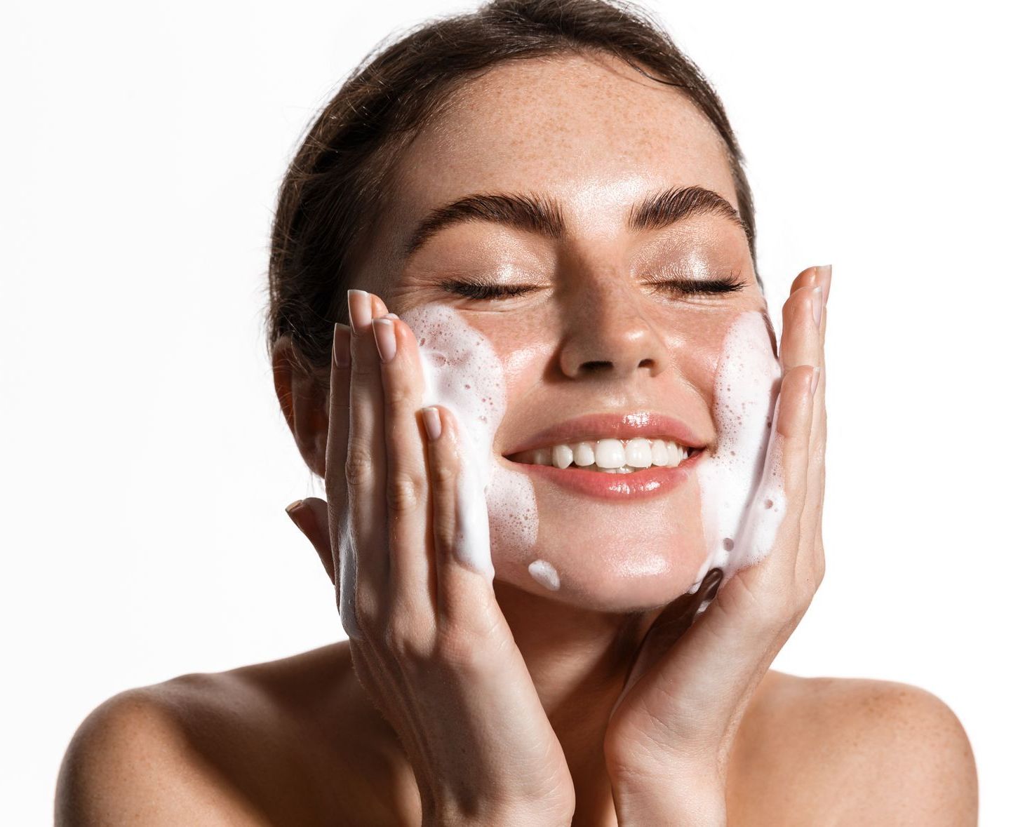 A woman is washing her face with soap and smiling.